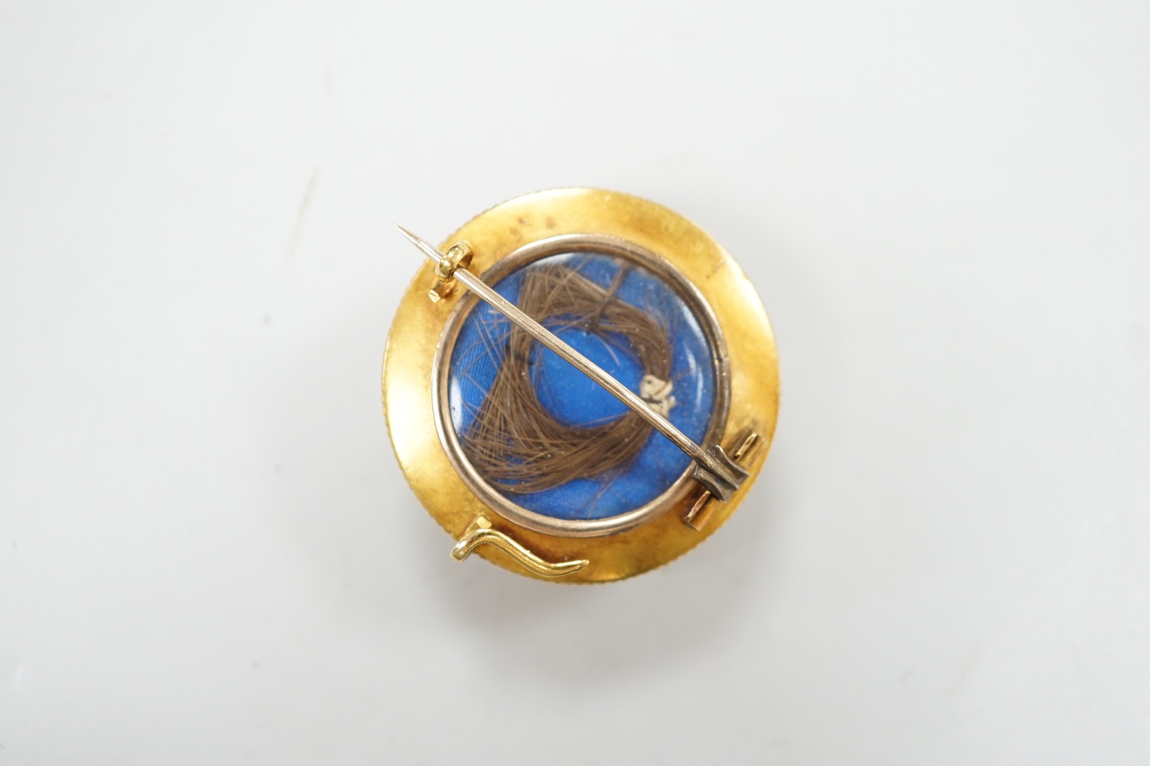 A cased Victorian yellow metal, enamel and split pearl set circular mourning pendant brooch, the glazed back with lock of hair beneath, diameter 34mm, gross weight 12.6 grams.